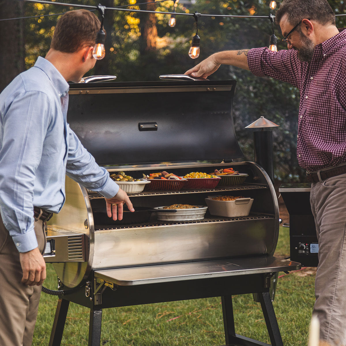 Two guys grilling a variety of meats on a backyard pellet grill